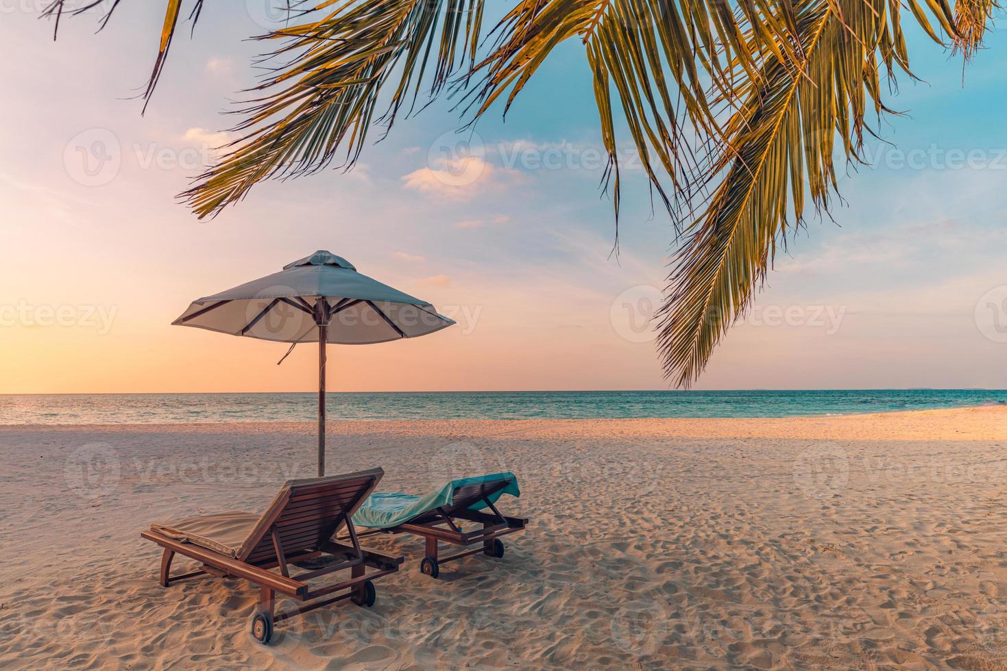 Le soleil couchant sur la plage. belle côte de l'île tropicale, deux chaises longues, parasol sous palmier. horizon de mer de sable, ciel de rêve coloré, calme et détente. paysage de plage de vacances d'été. complexe romantique pour couples photo