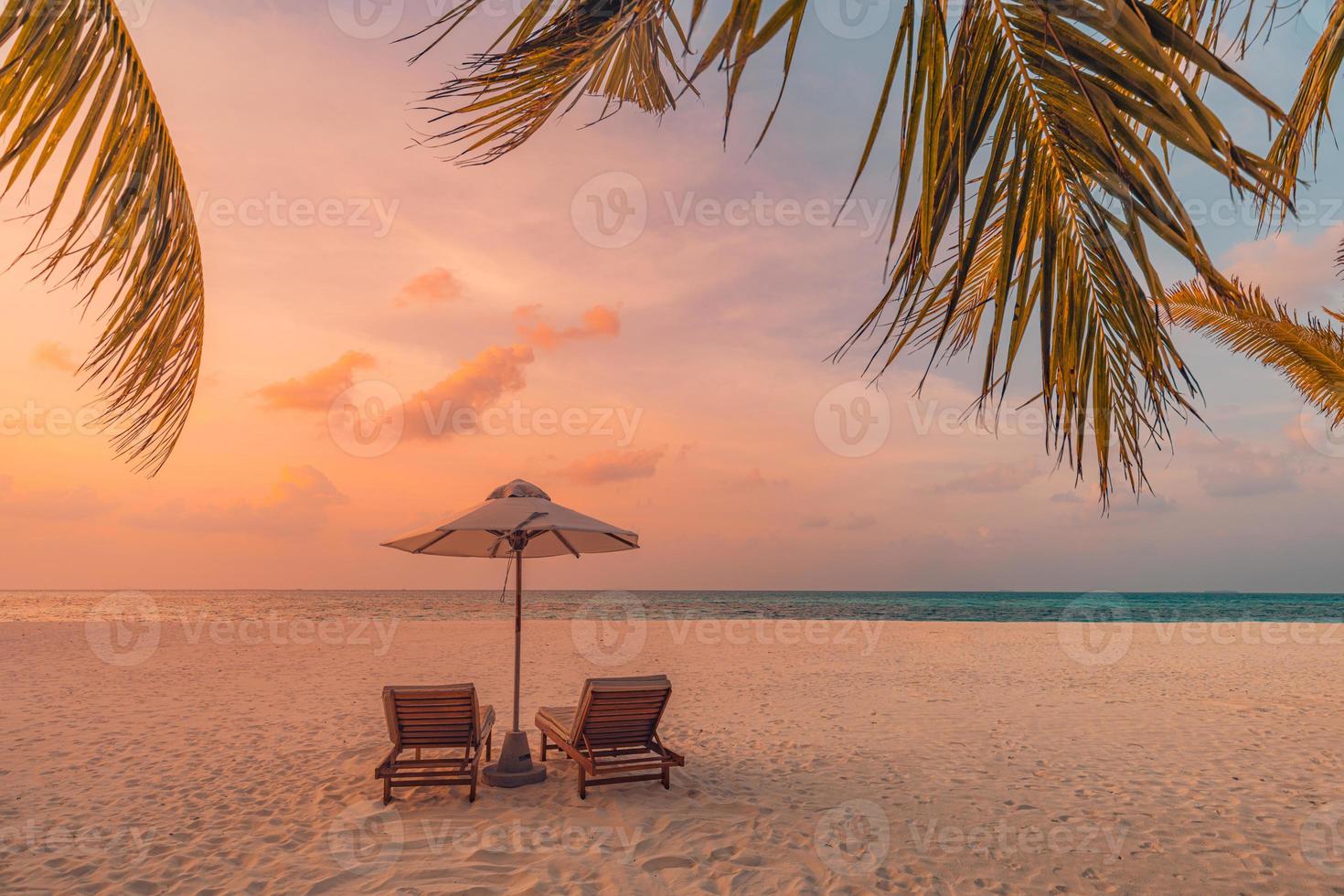 Le soleil couchant sur la plage. belle côte de l'île tropicale, deux chaises longues, parasol sous palmier. horizon de mer de sable, ciel de rêve coloré, calme et détente. paysage de plage de vacances d'été. complexe romantique pour couples photo