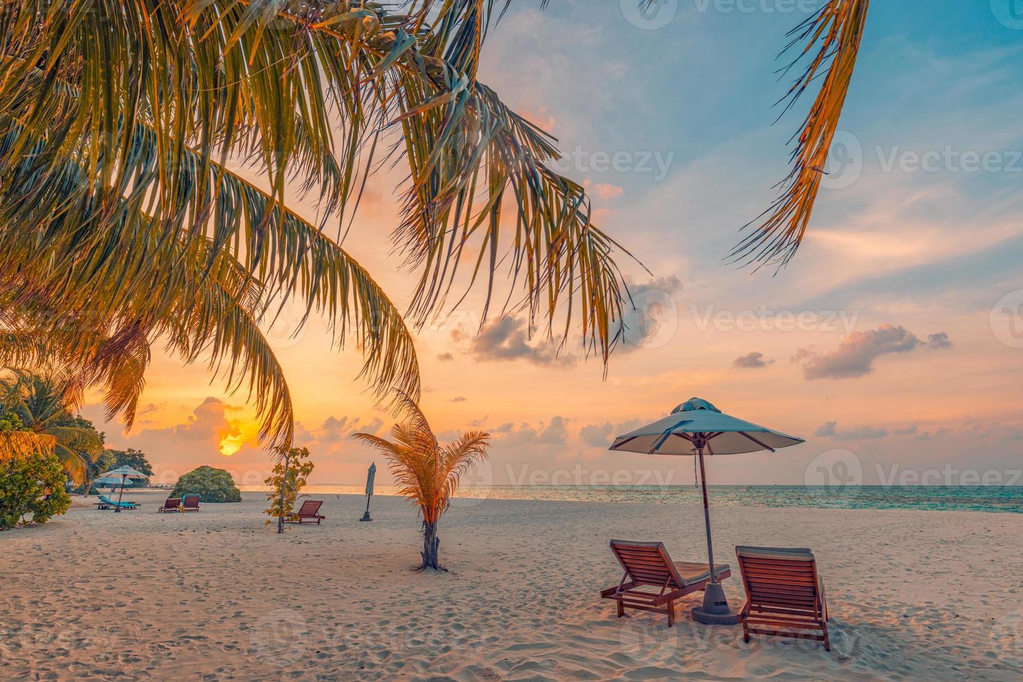 Le soleil couchant sur la plage. belle côte de l'île tropicale, deux chaises longues, parasol sous palmier. horizon de mer de sable, ciel de rêve coloré, calme et détente. paysage de plage de vacances d'été. complexe romantique pour couples photo