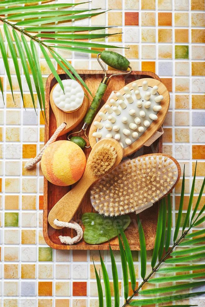 pots de crème pour les soins du visage et du corps, patchs dorés pour les yeux et sérum à l'or, masseur à rouleau de jade gau-sha et masseur et brosse pour le corps sur fond de mosaïque de carreaux photo