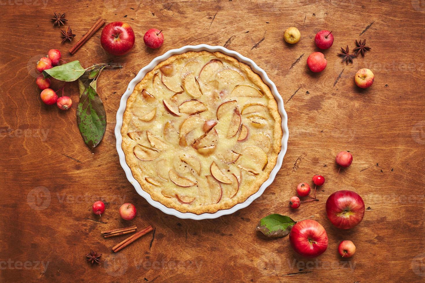 gâteau aux pommes fait maison avec de la crème sure, des pommes rouges, des pommettes et de la cannelle sur fond de bois, vue de dessus photo