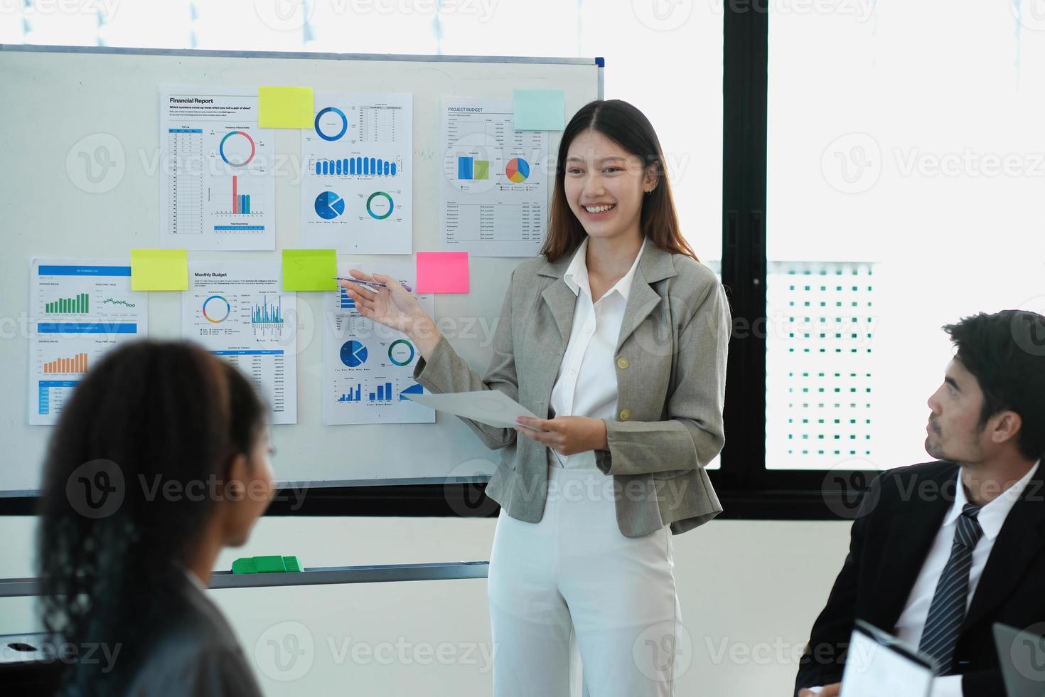 une femme responsable des opérations tient une présentation de réunion pour une équipe d'économistes. une femme asiatique utilise un tableau blanc numérique avec une analyse de la croissance, des graphiques, des statistiques et des données. les gens travaillent dans un bureau d'affaires. photo