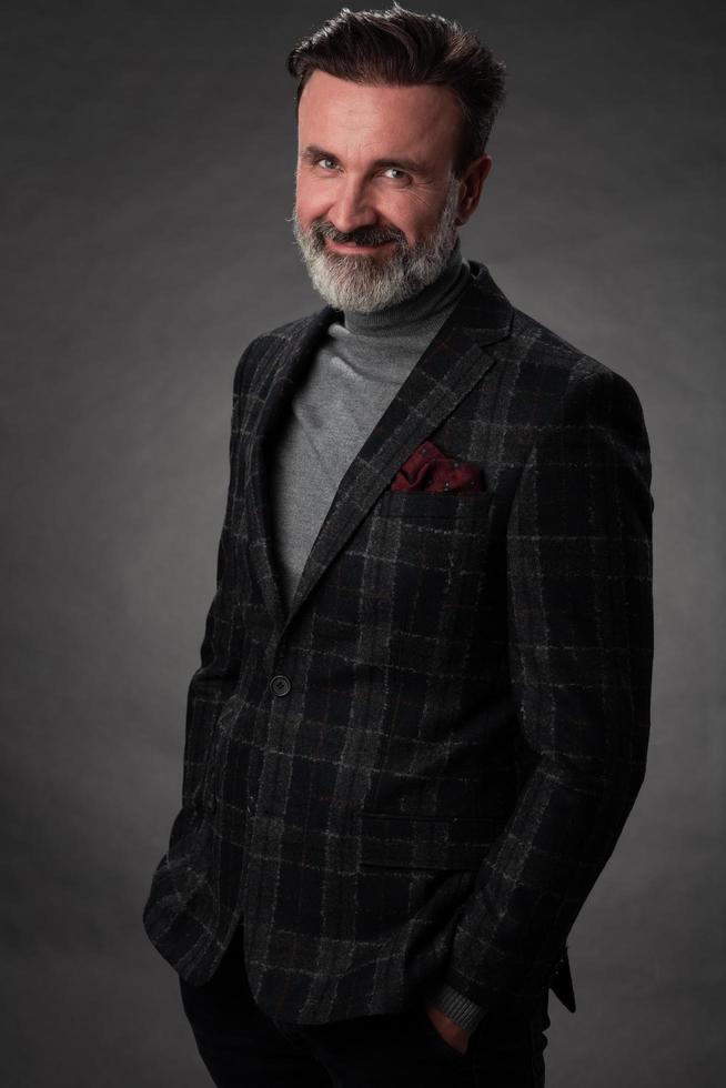 portrait d'un homme d'affaires senior élégant et élégant avec une barbe et des vêtements d'affaires décontractés en studio photo isolé sur fond sombre gesticulant avec les mains