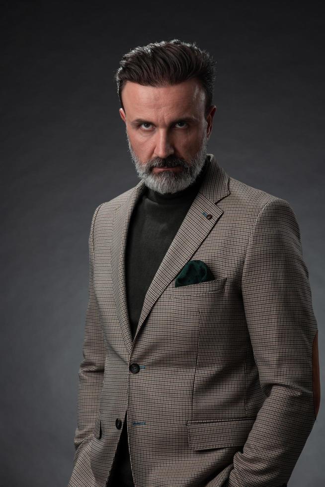 portrait d'un homme d'affaires senior élégant et élégant avec une barbe et des vêtements d'affaires décontractés en studio photo isolé sur fond sombre gesticulant avec les mains