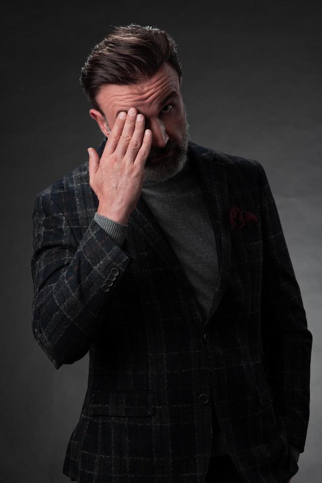 portrait d'un homme d'affaires senior élégant et élégant avec une barbe et des vêtements d'affaires décontractés en studio photo isolé sur fond sombre gesticulant avec les mains