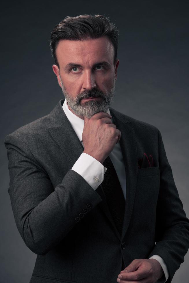 portrait d'un homme d'affaires senior élégant et élégant avec une barbe et des vêtements d'affaires décontractés en studio photo isolé sur fond sombre gesticulant avec les mains