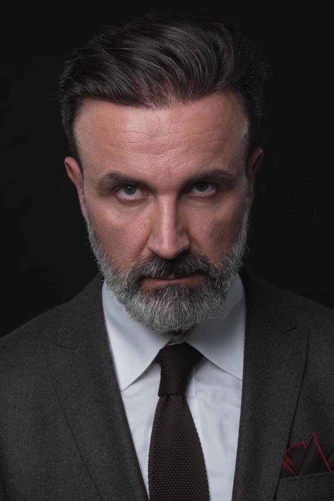 portrait d'un homme d'affaires senior élégant et élégant avec une barbe et des vêtements d'affaires décontractés en studio photo isolé sur fond sombre gesticulant avec les mains