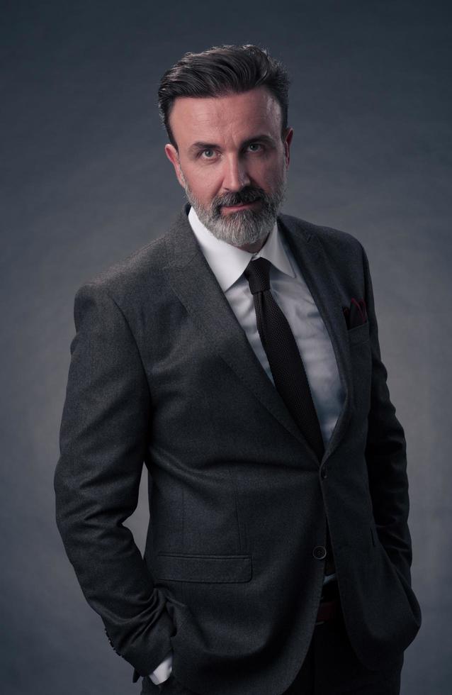 portrait d'un homme d'affaires senior élégant et élégant avec une barbe et des vêtements d'affaires décontractés en studio photo isolé sur fond sombre gesticulant avec les mains