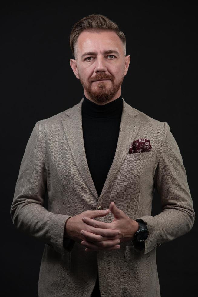 portrait d'un homme d'affaires senior élégant et élégant avec une barbe et des vêtements d'affaires décontractés en studio photo isolé sur fond sombre gesticulant avec les mains