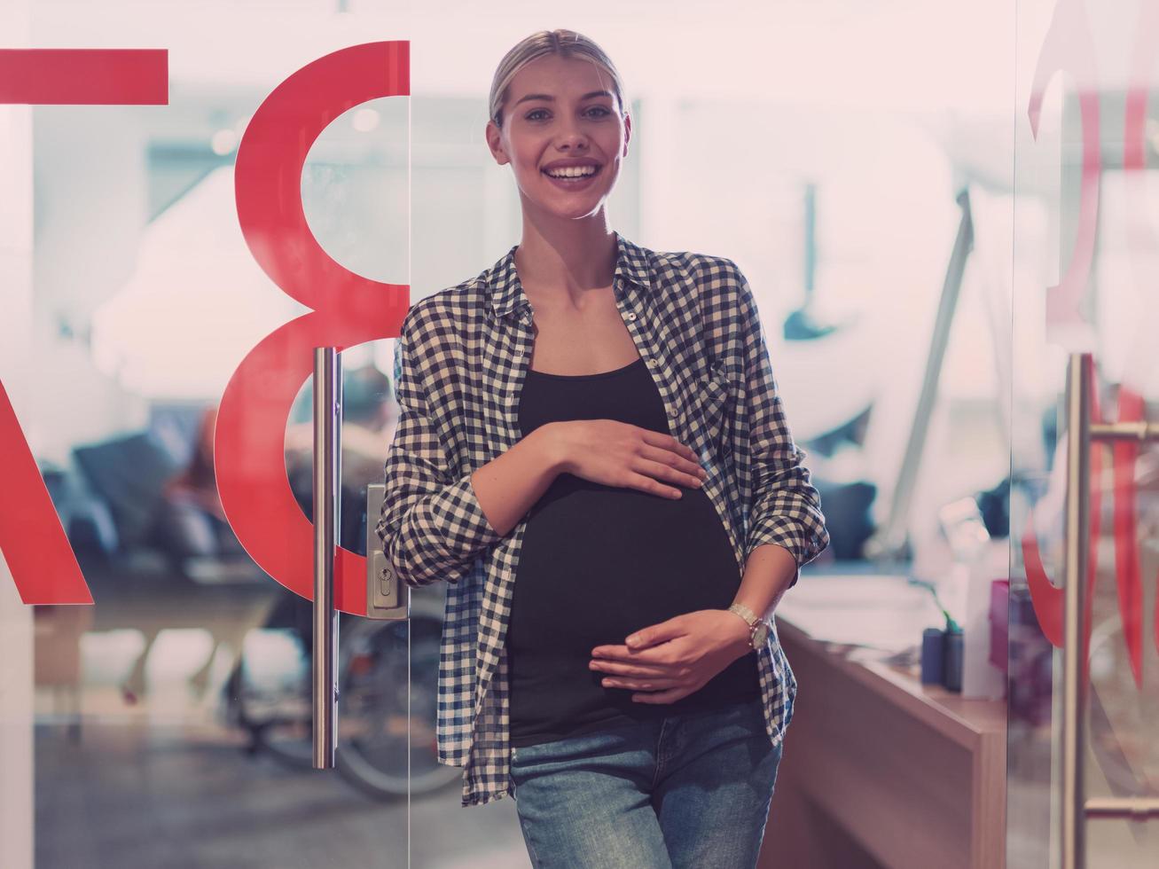 portrait d'une femme d'affaires enceinte tenant doucement le ventre dans un bureau moderne photo