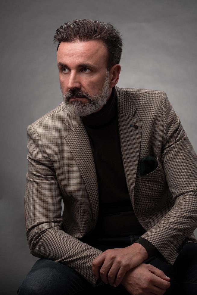 portrait d'un homme d'affaires senior élégant et élégant avec une barbe et des vêtements d'affaires décontractés en studio photo isolé sur fond sombre gesticulant avec les mains