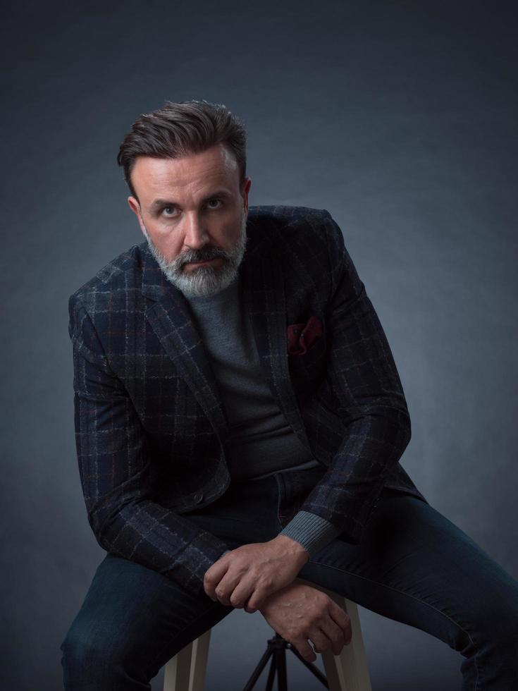 portrait d'un homme d'affaires adulte portant un costume à la mode et assis dans un studio moderne sur une chaise élégante sur fond noir photo