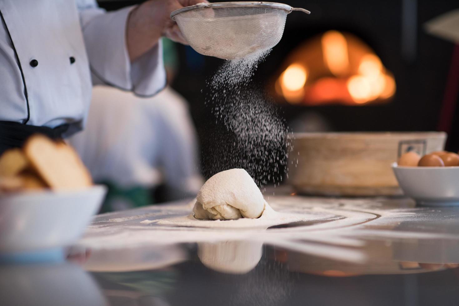 chef saupoudrant de farine sur la pâte à pizza fraîche photo