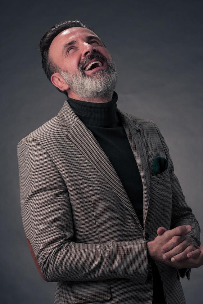 portrait d'un homme d'affaires senior élégant et élégant avec une barbe et des vêtements d'affaires décontractés en studio photo isolé sur fond sombre gesticulant avec les mains