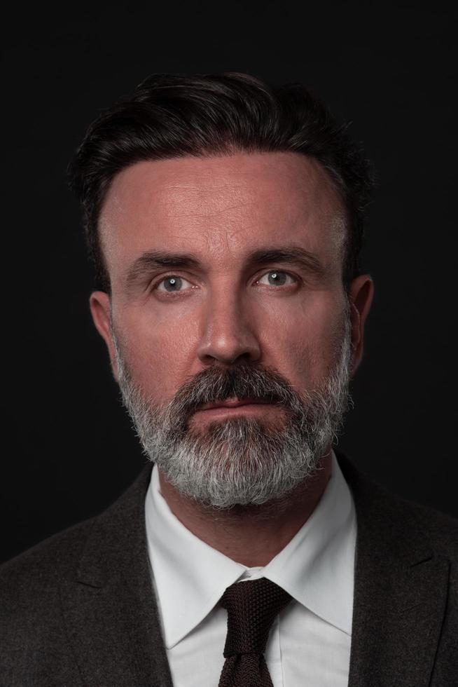 portrait d'un homme d'affaires senior élégant et élégant avec une barbe et des vêtements d'affaires décontractés en studio photo isolé sur fond sombre gesticulant avec les mains