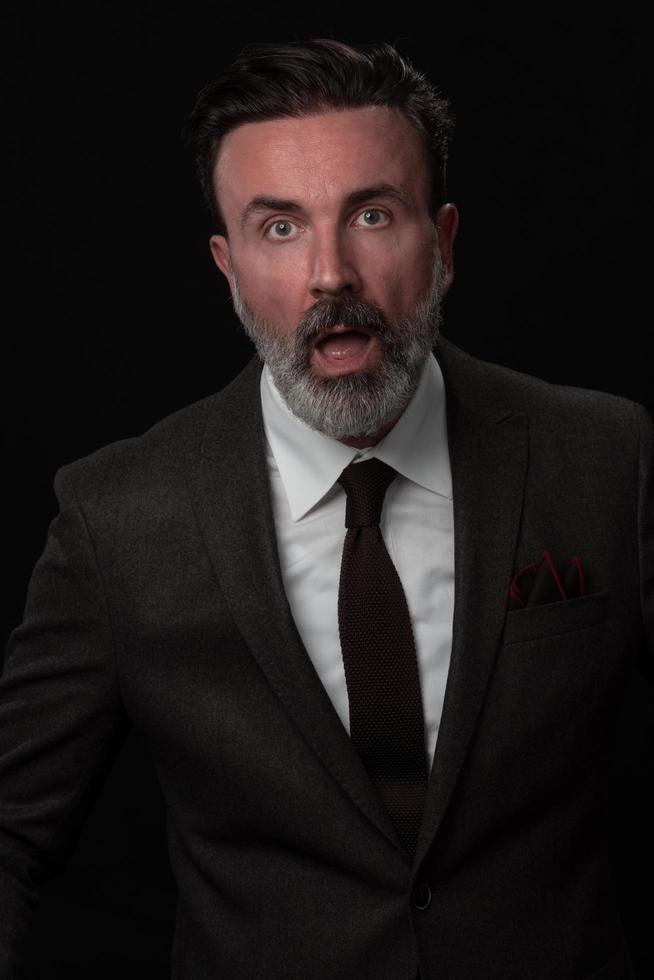 portrait d'un homme d'affaires senior élégant et élégant avec une barbe et des vêtements d'affaires décontractés en studio photo isolé sur fond sombre gesticulant avec les mains