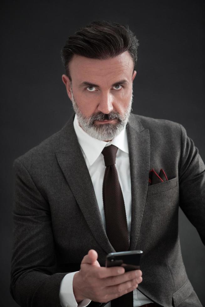 portrait d'un homme d'affaires adulte portant un costume à la mode et assis dans un studio moderne sur une chaise élégante sur fond noir photo