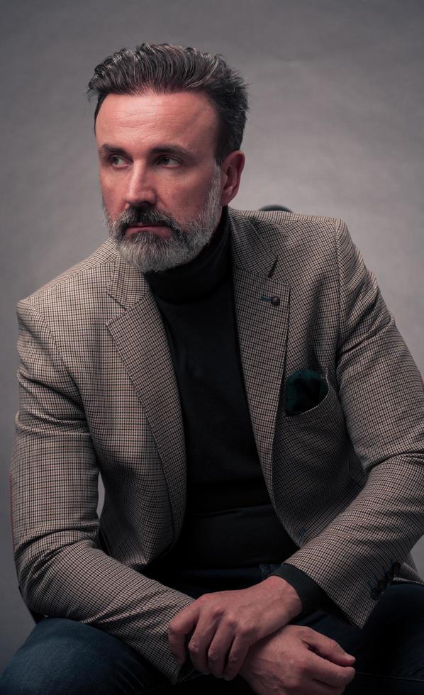 portrait d'un homme d'affaires senior élégant et élégant avec une barbe et des vêtements d'affaires décontractés en studio photo isolé sur fond sombre gesticulant avec les mains