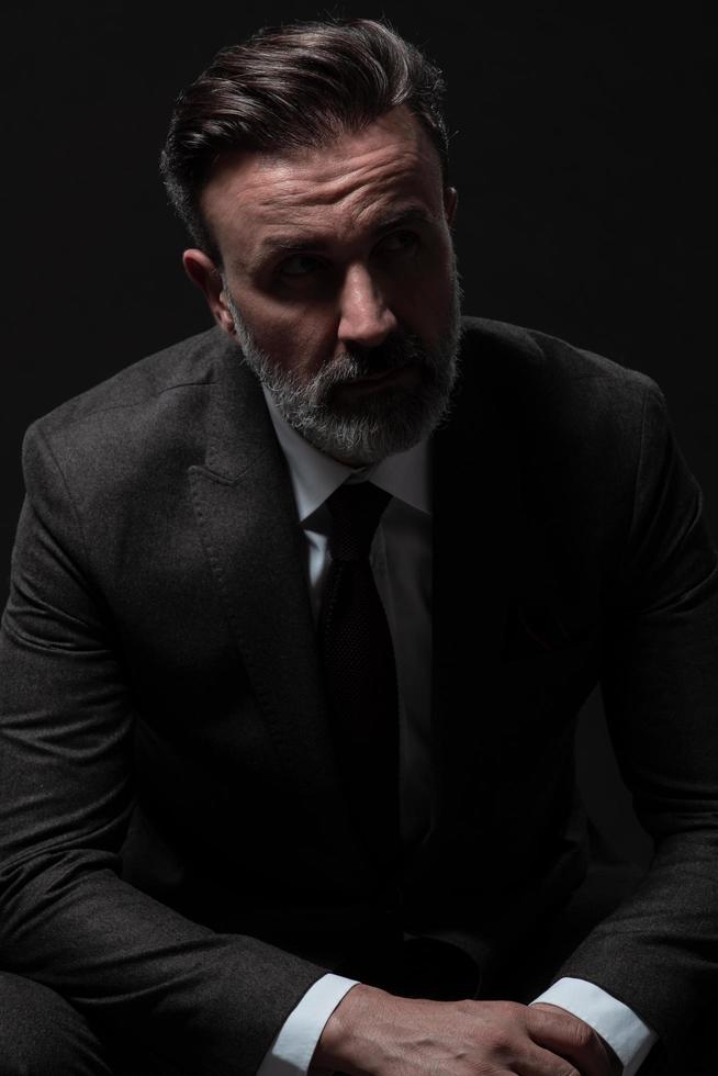 portrait d'un homme d'affaires senior élégant et élégant avec une barbe et des vêtements d'affaires décontractés en studio photo isolé sur fond sombre gesticulant avec les mains