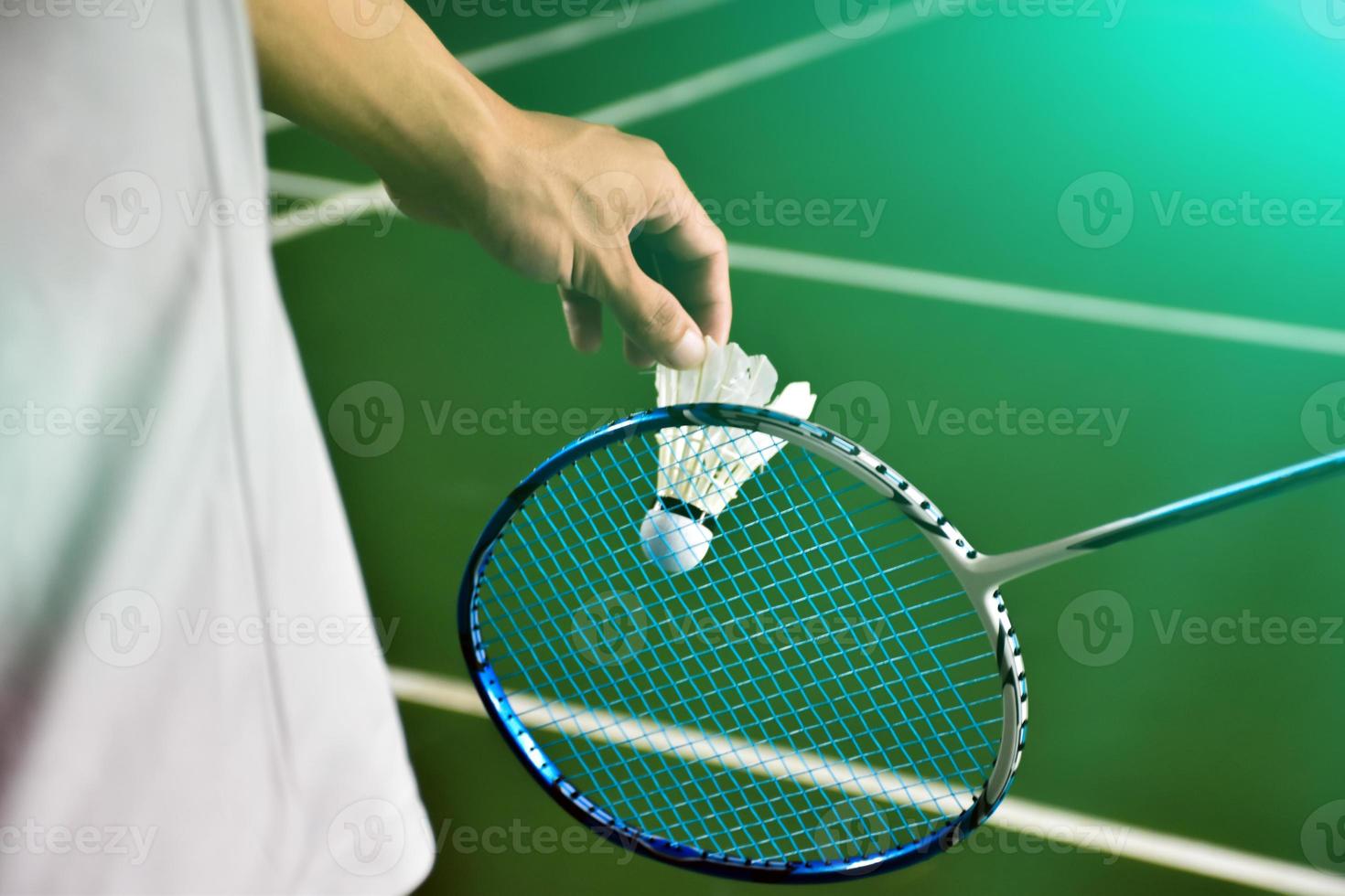 le joueur de badminton tient une raquette et un volant crème blanc devant le filet avant de le servir de l'autre côté du terrain. photo