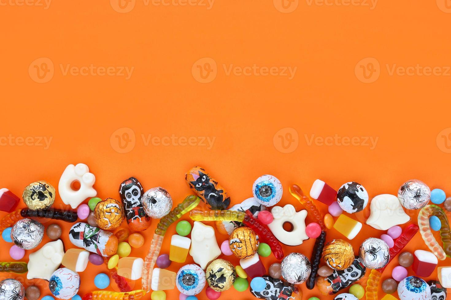 fond orange avec espace de copie, bonbons assortis d'halloween en bas - chocolats traditionnels aux globes oculaires, vers de gelée, fantômes. bonne vente de vacances d'halloween et concept trick-or-treat. photo
