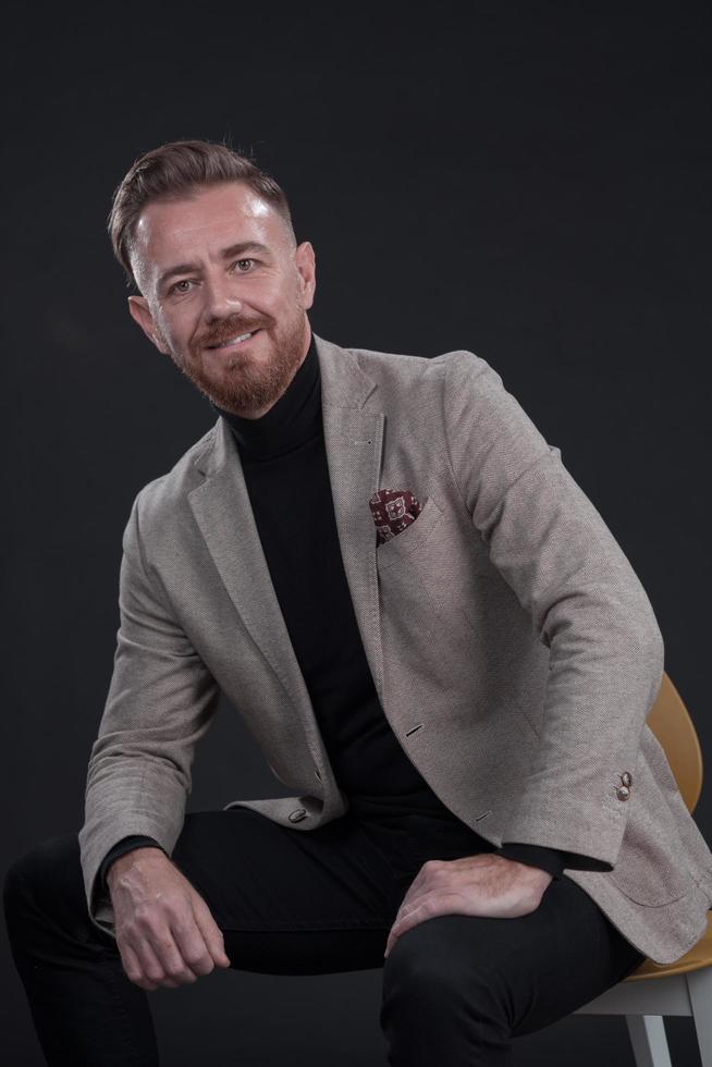 portrait d'un homme d'affaires adulte portant un costume à la mode et assis dans un studio moderne sur une chaise élégante sur fond noir photo