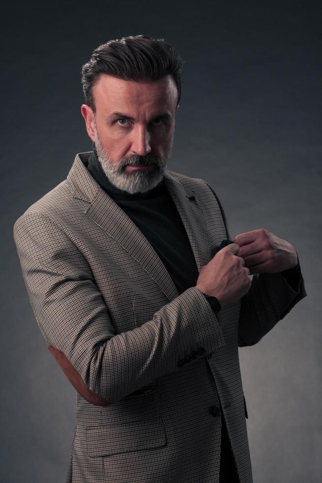 portrait d'un homme d'affaires senior élégant et élégant avec une barbe et des vêtements d'affaires décontractés en studio photo isolé sur fond sombre gesticulant avec les mains