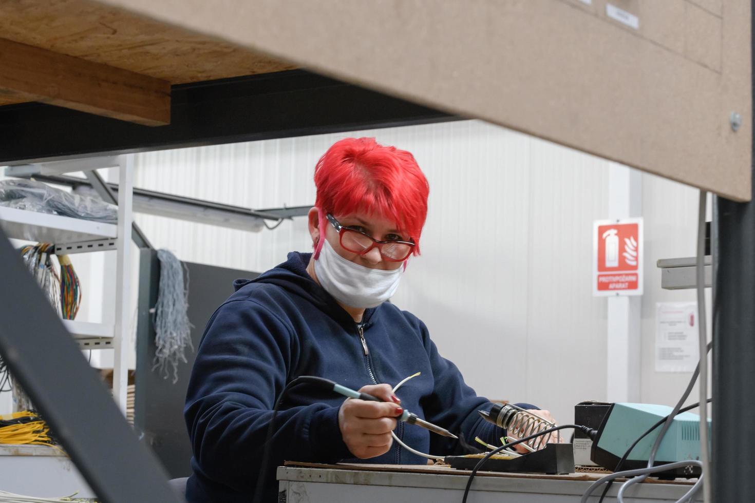 travailleur industriel portant un masque facial en raison d'une pandémie de coronavirus soude les câbles de l'équipement de production d'usine photo