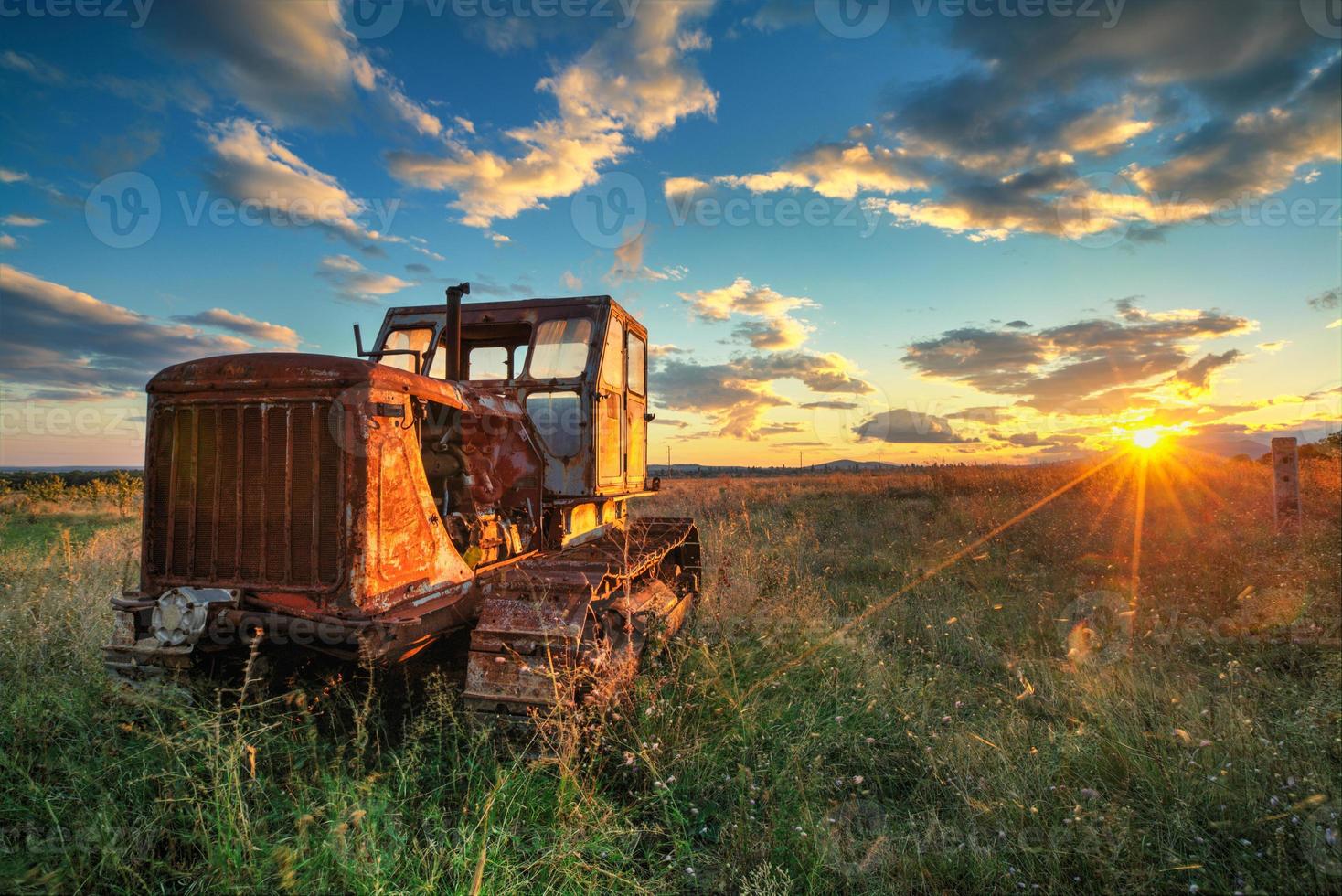 vieux tracteur rouillé dans un champ au coucher du soleil photo
