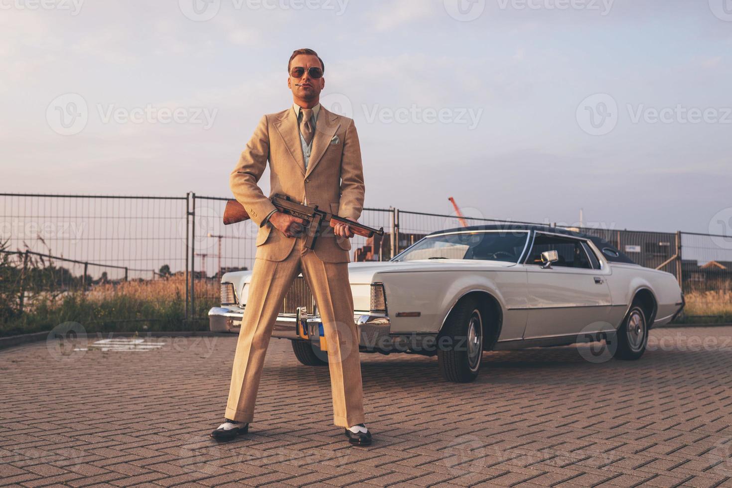gangster rétro des années 1970 tenant un pistolet debout devant la voiture. photo