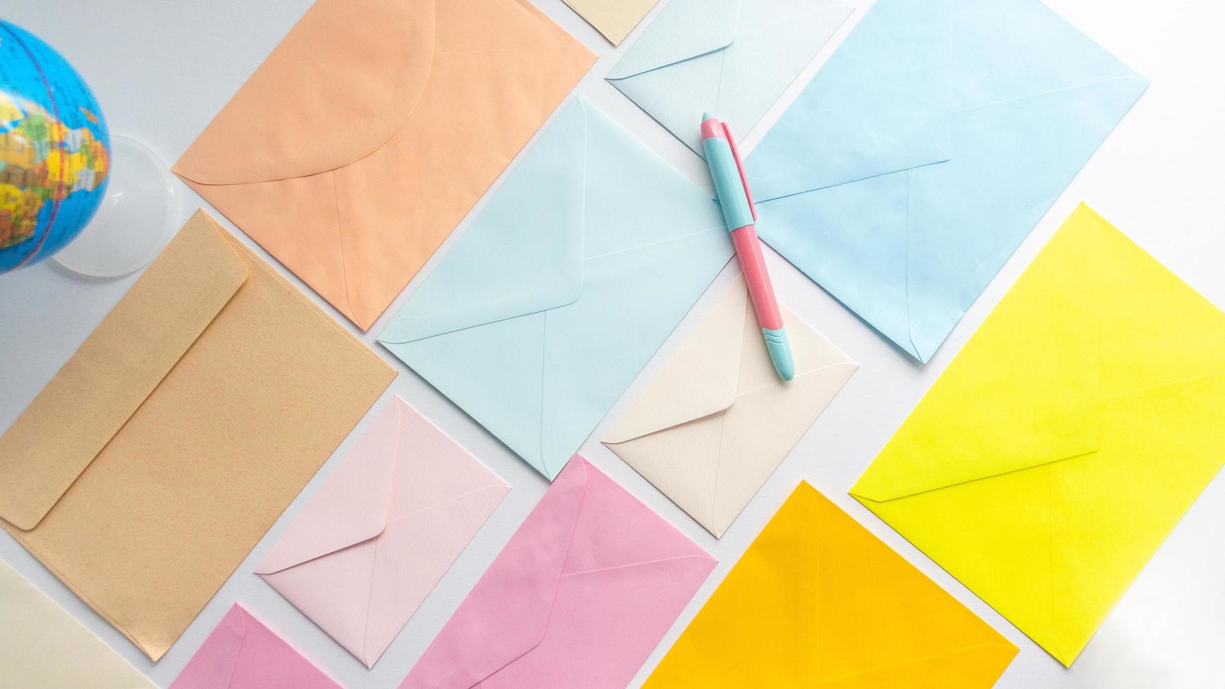 les enveloppes aux couleurs pastel s'alignent en oblique avec un globe dans le coin gauche et un stylo photo