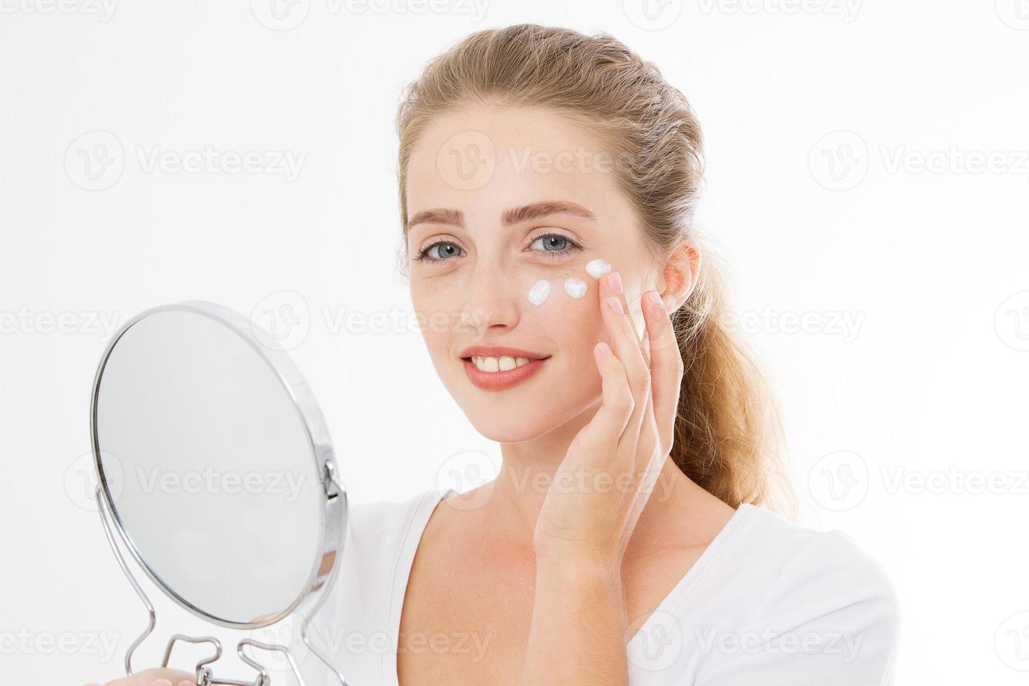 jeune femme blonde caucasienne avec miroir et crème hydratante pour les soins de la peau du visage sur le visage isolé sur fond blanc. concept anti-âge et spa. maquillage et beauté de la nature. copie espace photo