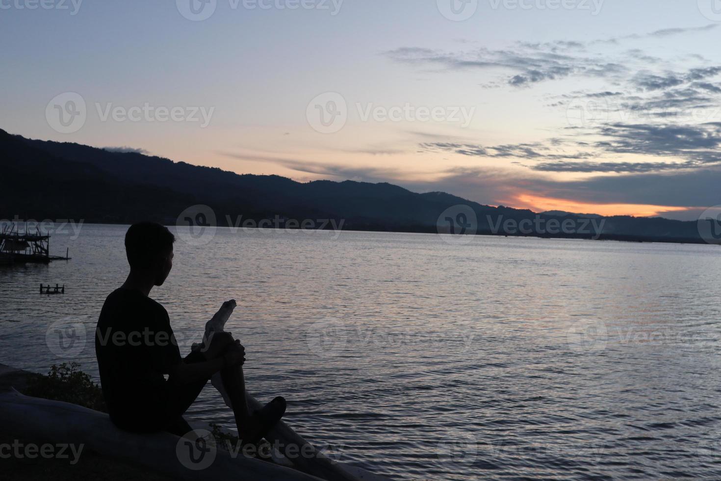 silhouette d'un jeune homme debout au bord du lac en profitant du coucher de soleil. atmosphère paisible dans la nature photo