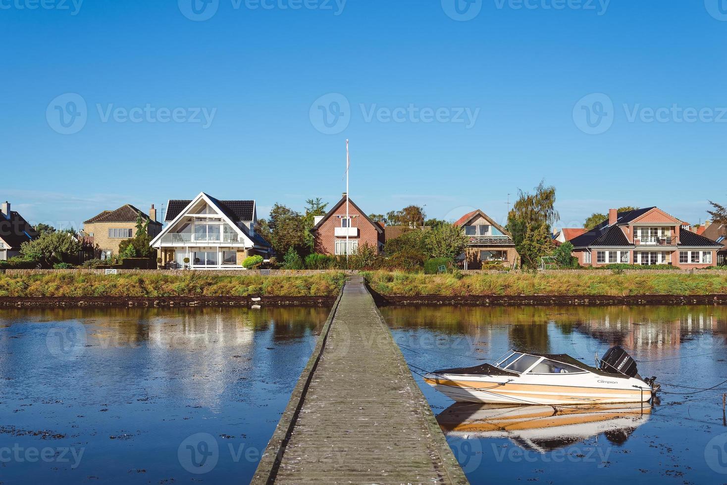 village moderne près de dragor, danemark - 21 septembre 2015. maisons scandinaves de cottage, quai en bois et bateau à moteur reflétés sur l'eau du détroit d'oresund. photo