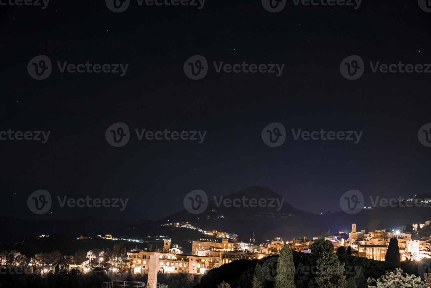 ville côtière illuminée et mont etna avec ciel sombre en arrière-plan la nuit photo