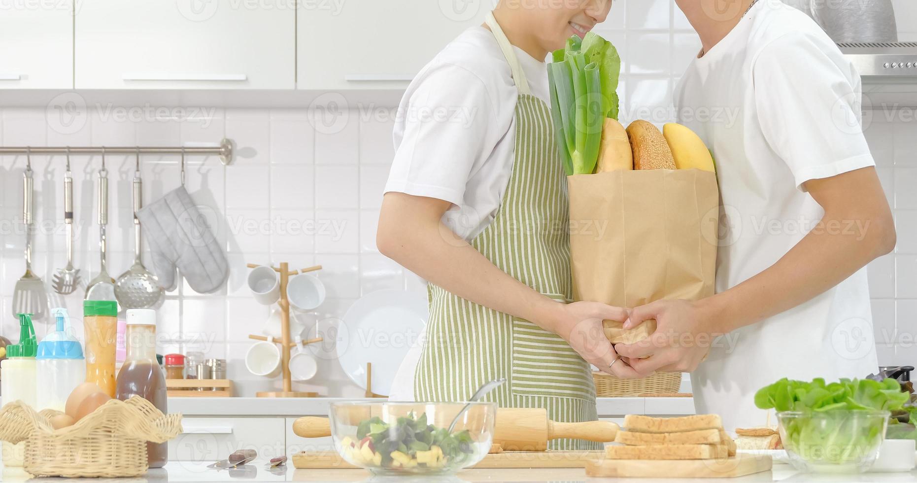 concept de vie domestique de jeune couple lgbt. demi-portrait jeune couple d'hommes lgbt heureux tenant un sac à provisions avec des ingrédients ensemble pendant la cuisson dans la cuisine. mise au point sélective et espace de copie. photo