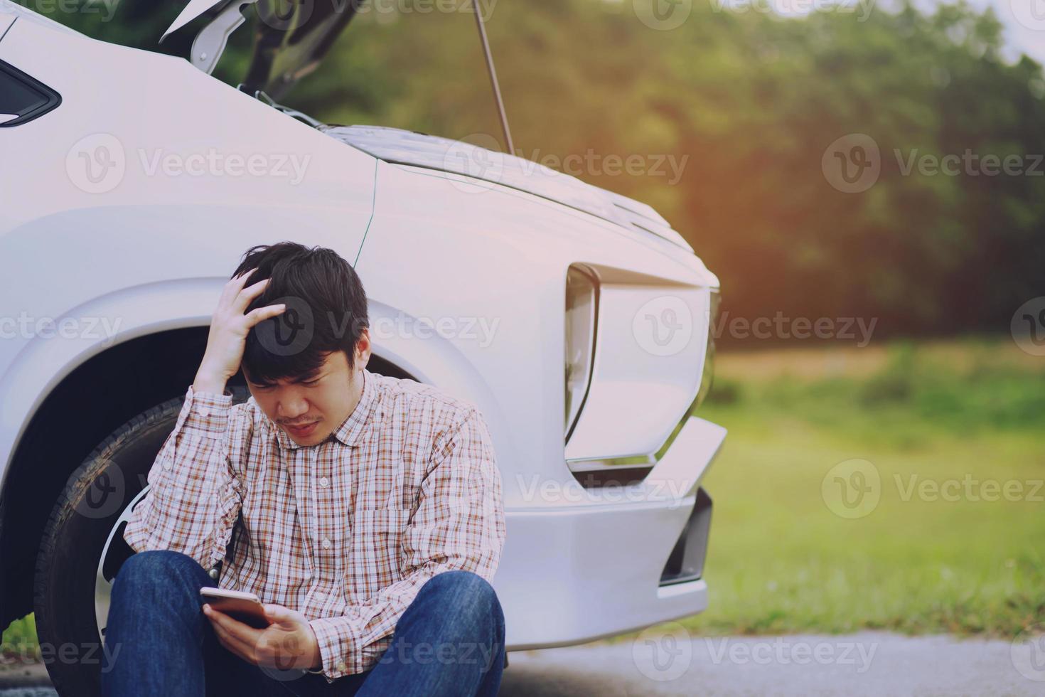 gros plan la main d'un homme d'affaires à l'aide d'un téléphone intelligent mobile appeler un mécanicien automobile demander de l'aide parce que la voiture a cassé le bord de la route. personnes voyage amis s'asseoir attendre à côté d'une voiture cassée photo