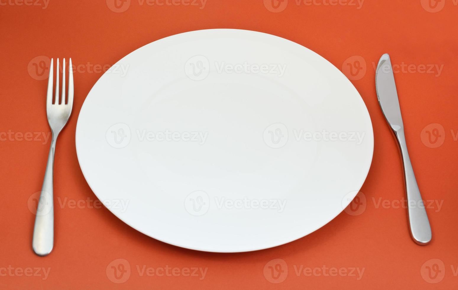 assiette en porcelaine vide avec fourchette et couteau sur rouge photo