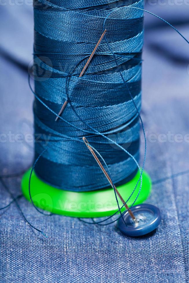 bobine de fil avec aiguilles, bouton sur textile bleu photo