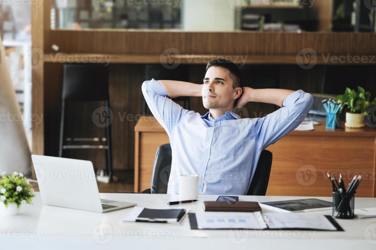 directeur marketing masculin se reposant et souriant tout en travaillant pour réduire la somnolence avant d'utiliser des ordinateurs, des ipads et des supports marketing. photo