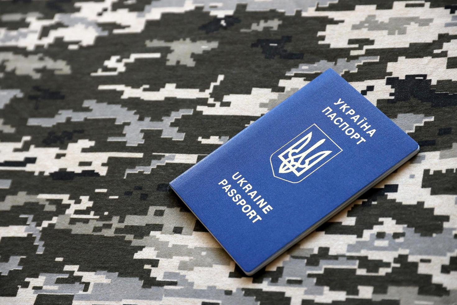 sumy, ukraine - 20 mars 2022 passeport étranger ukrainien sur tissu avec texture de camouflage pixelisé militaire. tissu avec motif camouflage en formes de pixels gris, marron et vert et identifiant ukrainien photo