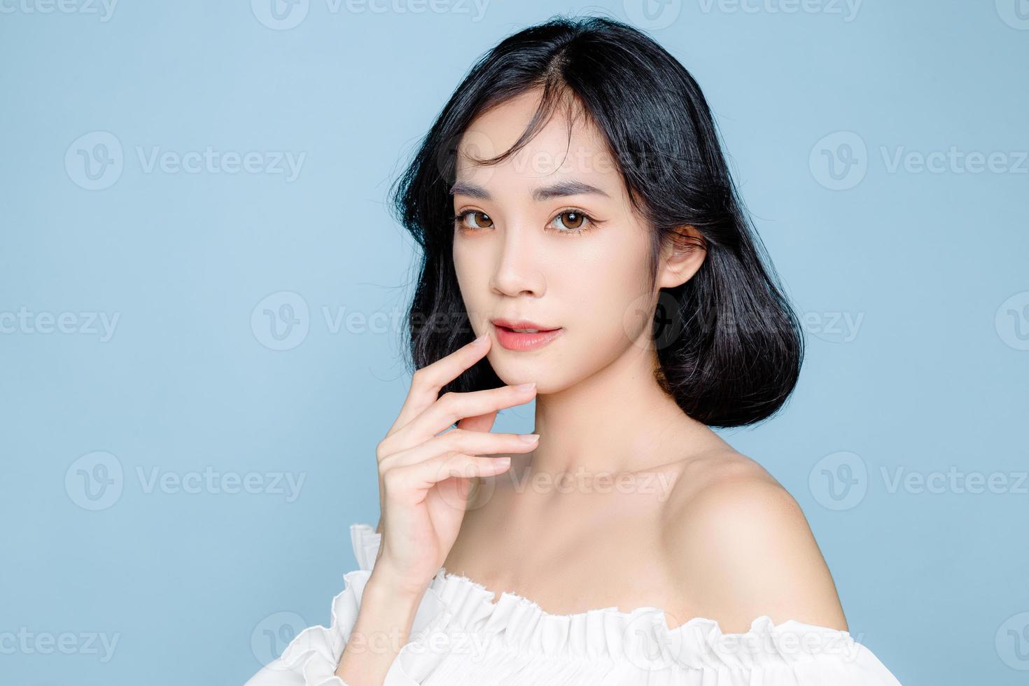 femme asiatique cheveux courts avec une peau fraîche parfaite et propre. modèle féminin mignon avec maquillage naturel et yeux pétillants sur fond bleu isolé. soin du visage, cosmétologie, concept de beauté. photo