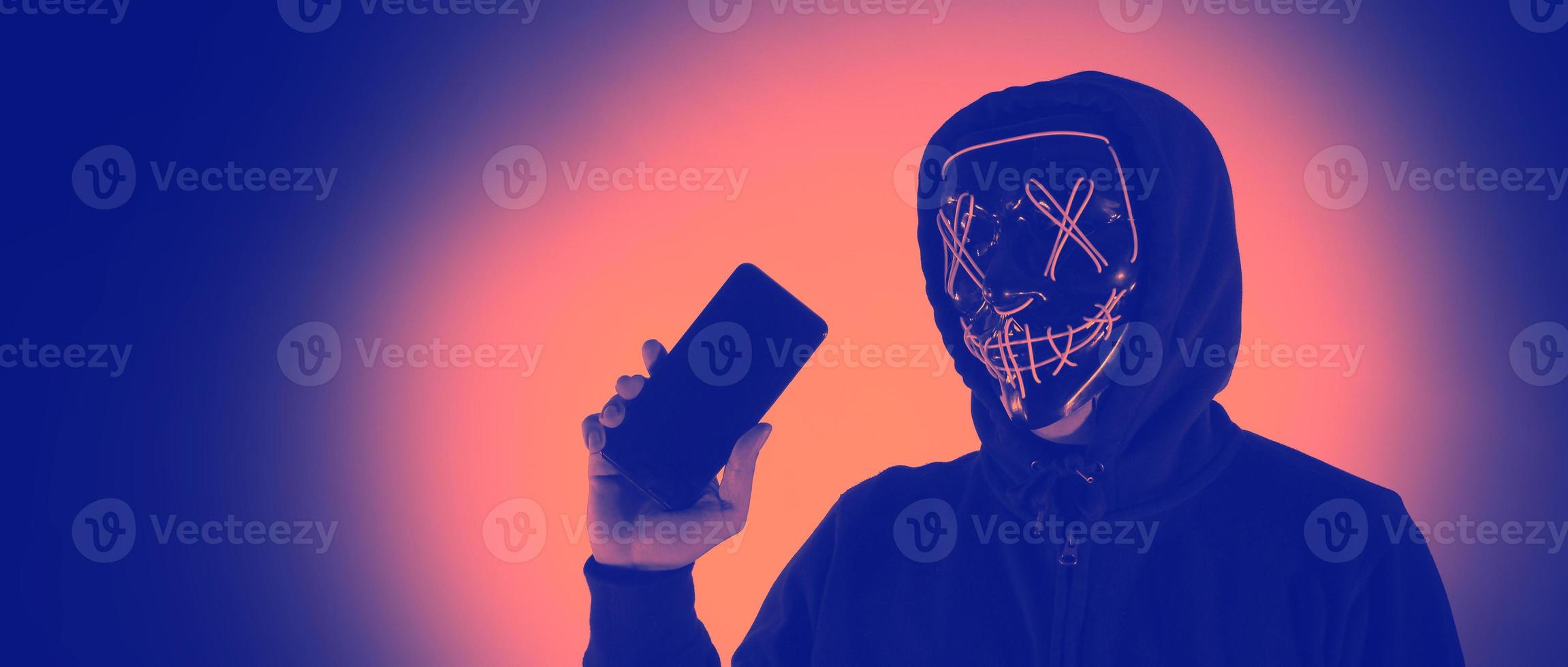 concept de sécurité numérique. pirate anonyme avec masque tenant un smartphone piraté. photo