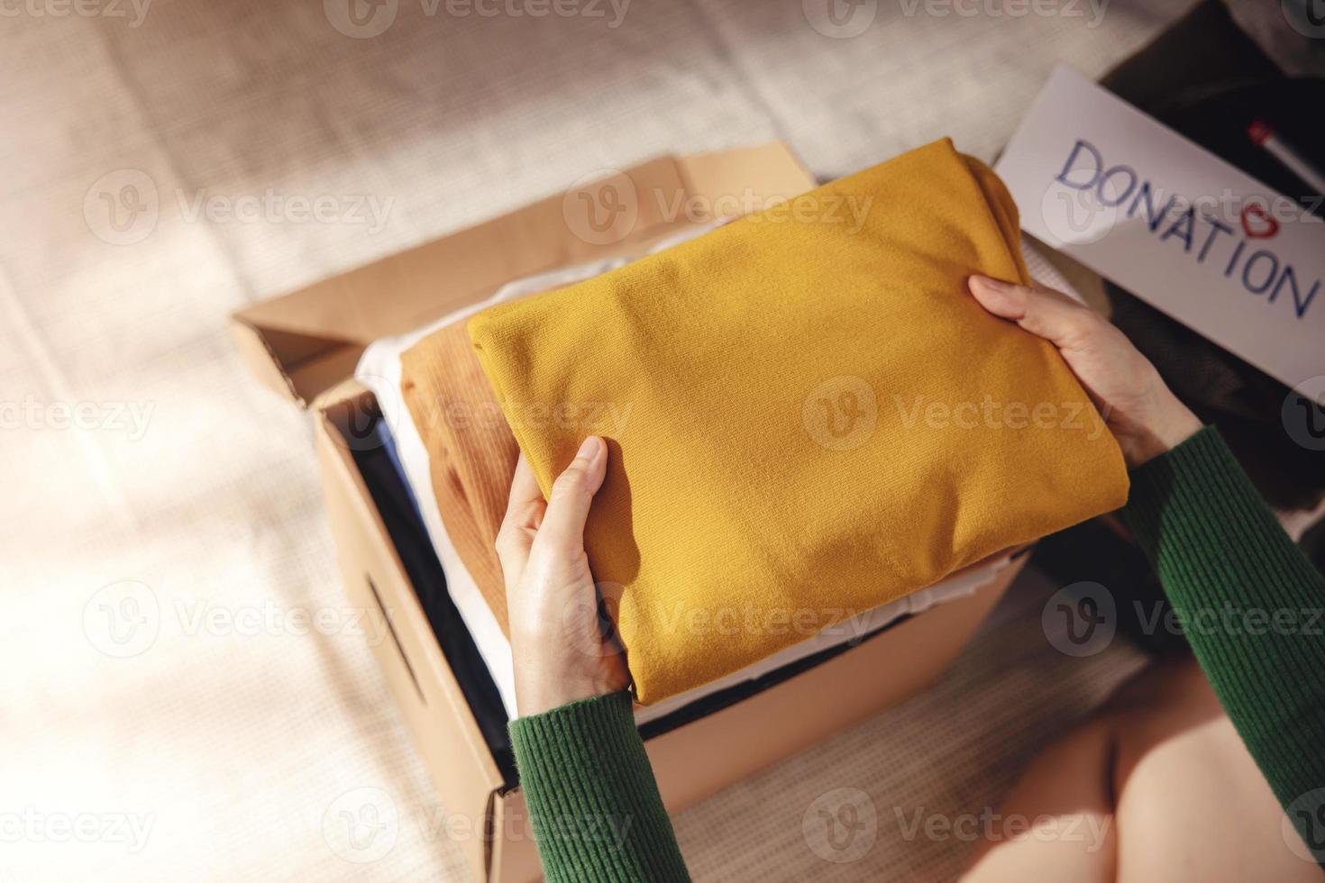 concept de don de vêtements. boîte de tissu avec étiquette de don. femme préparant un vieux vêtement usagé à la maison. vue de dessus photo