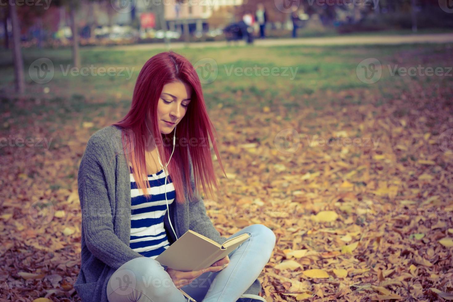 belle femme rousse relaxante avec livre et musique dans le parc. photo