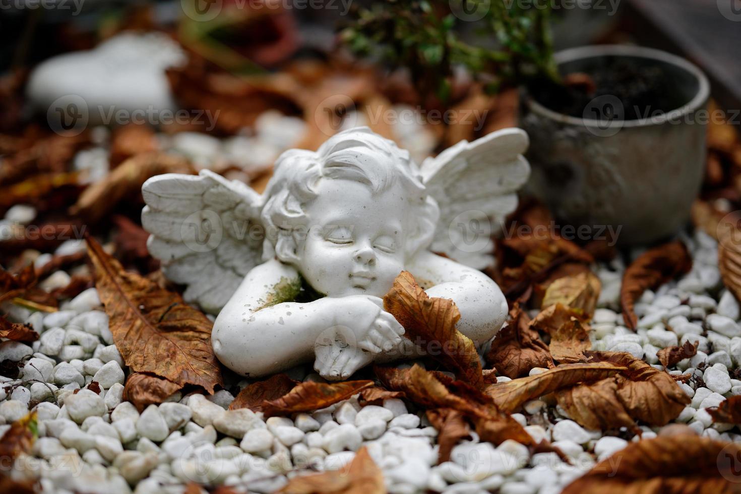 une petite figure d'ange dort sur une tombe avec des feuilles d'automne photo