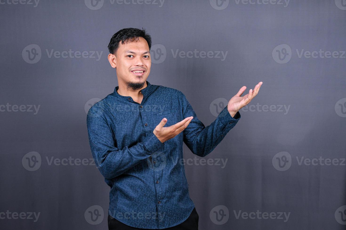jeune homme asiatique isolé sur fond gris pointant vers le côté pour présenter un produit photo