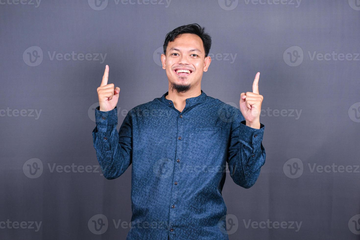 jeune homme asiatique isolé sur fond gris pointant vers le côté pour présenter un produit photo