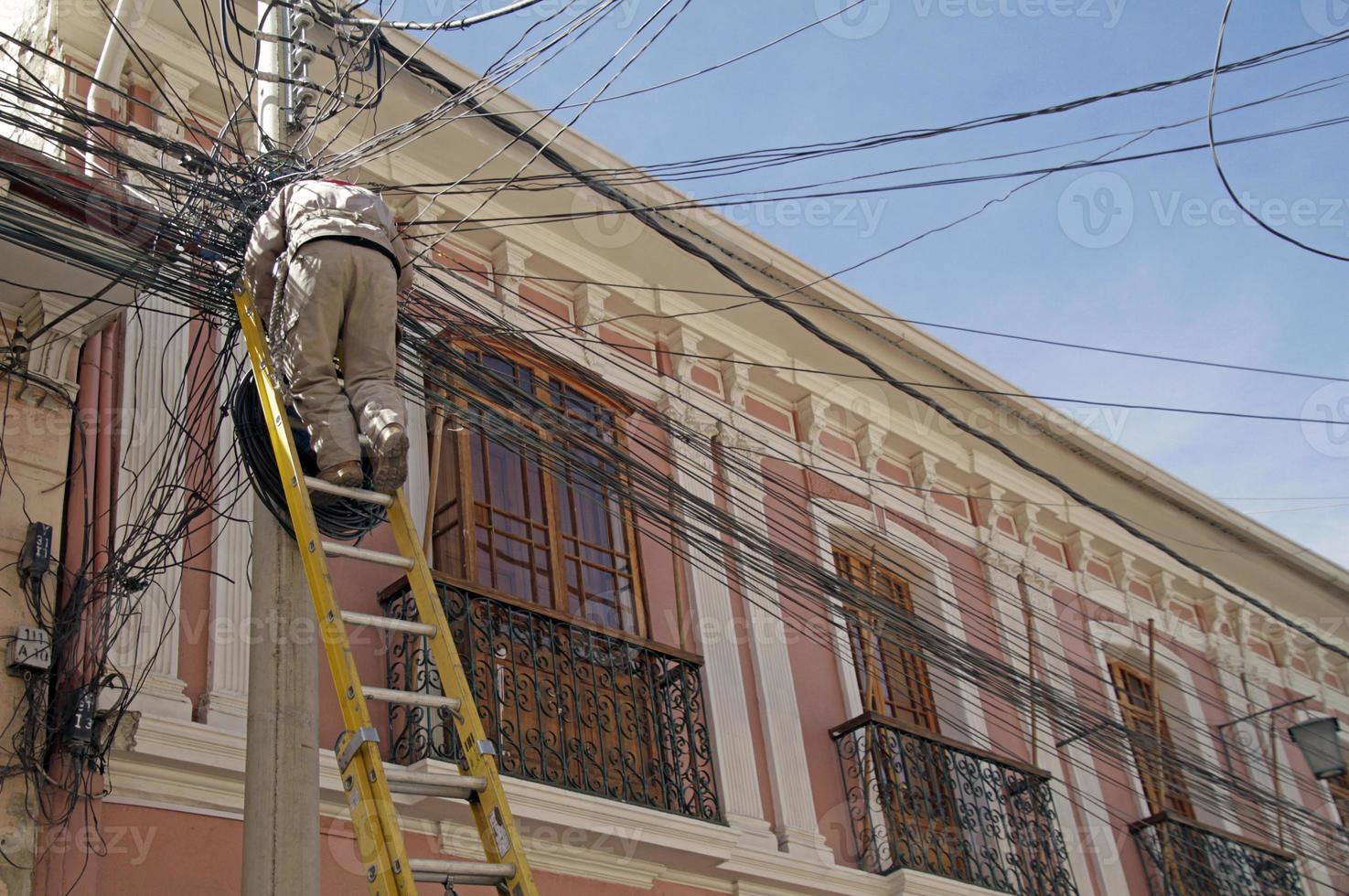 Travailleur sur une échelle réparant un contact au milieu de lignes électriques enchevêtrées attachées à un réverbère à la paz, en bolivie photo