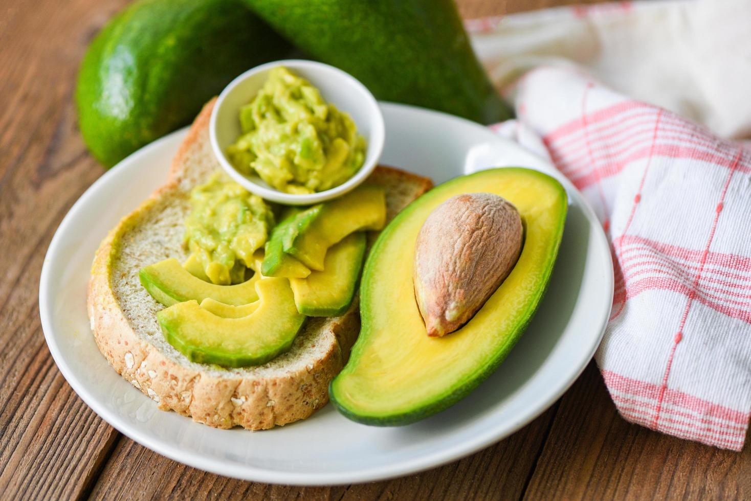 La moitié de l'avocat et la purée de trempette à l'avocat sur fond de plaque blanche concept d'aliments sains fruits - toast à l'avocat photo